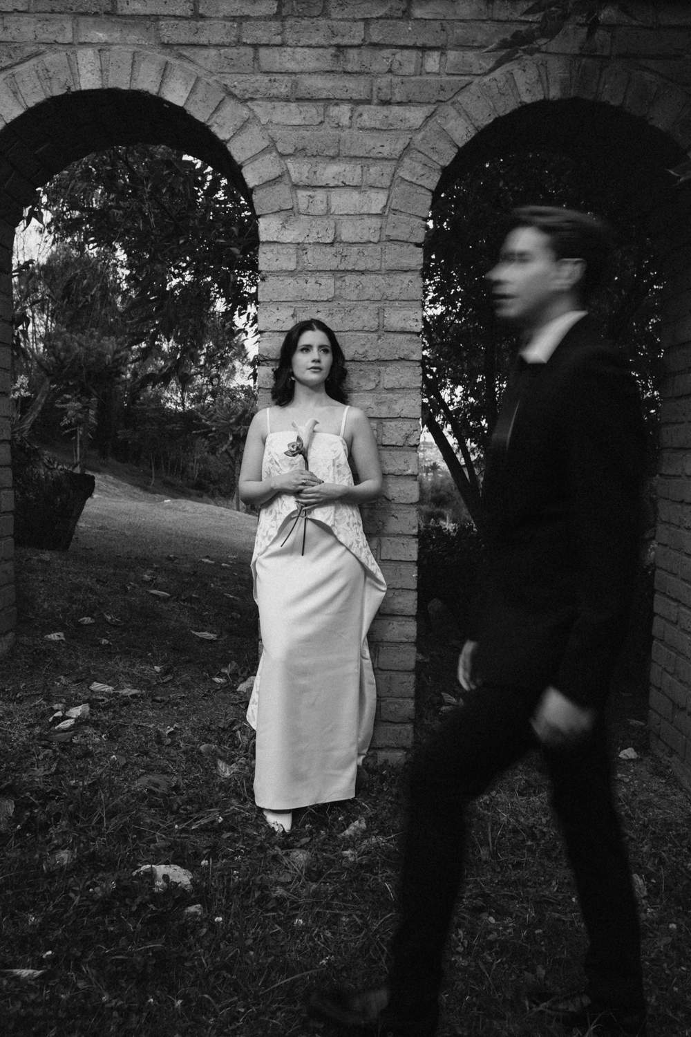 Retrato editorial en blanco y negro de los novios bajo un arco de ladrillo